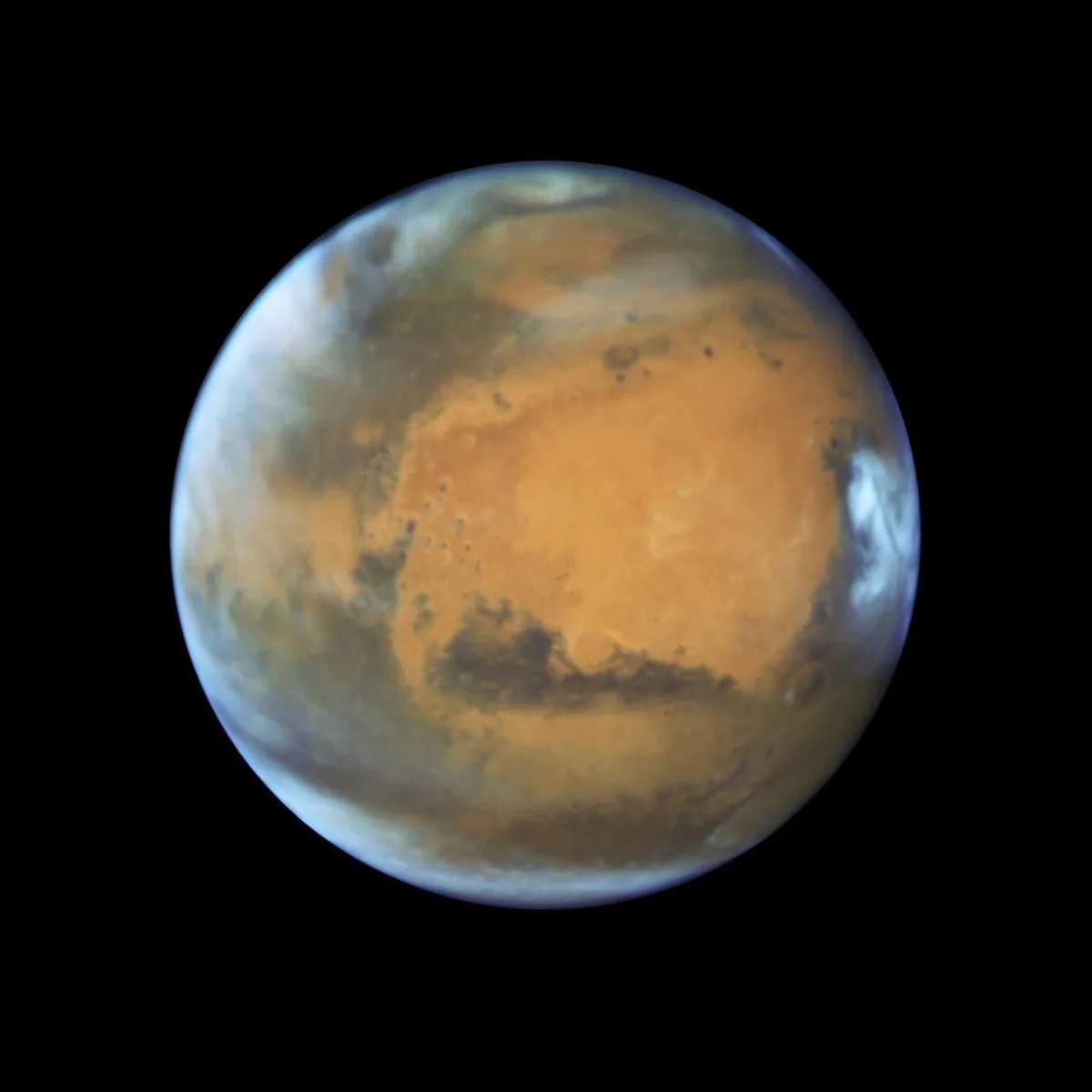 Rötliche Planetenscheibe des Mars mit hellen Wolken und dunklen Oberflächenregionen